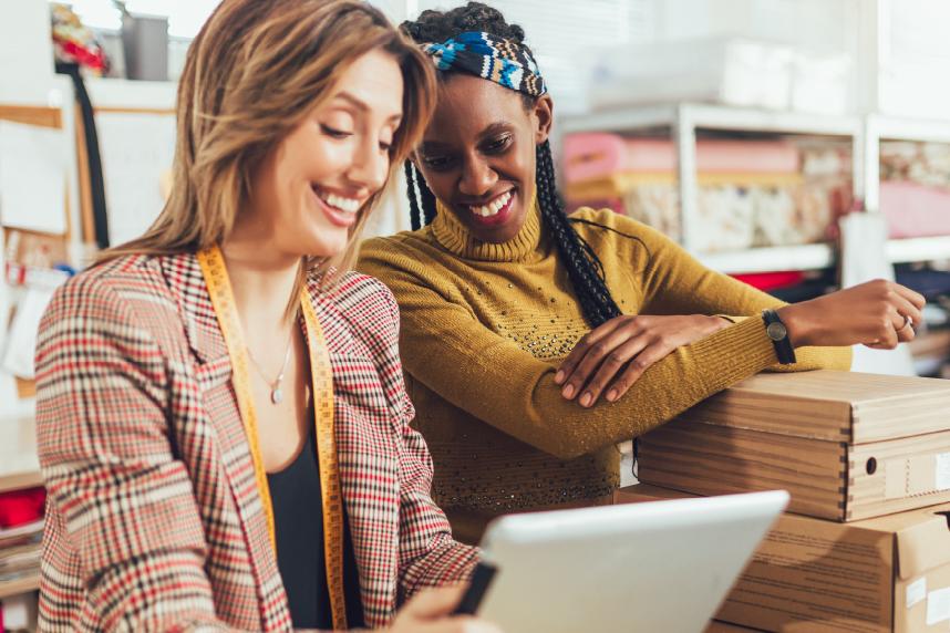 Two women looking at tablet while boxing up their products