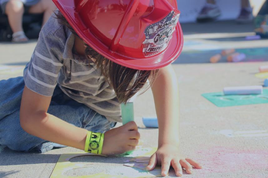 Little girl in fireman's helmet, drawing on sidewalk with chalk