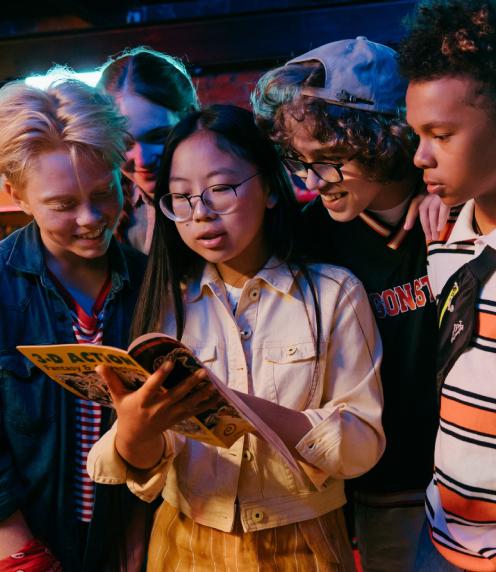 Teens gathering around another teenager to look at an open comic book