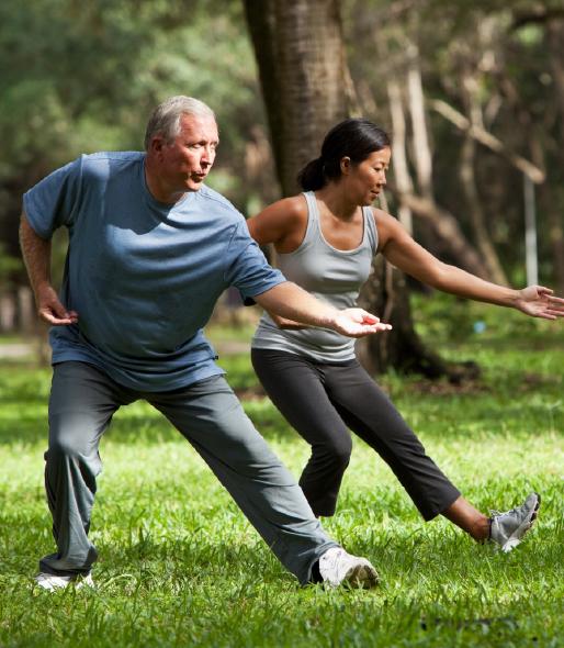 A man and a woman doing Tai Chi outside in a wooden area