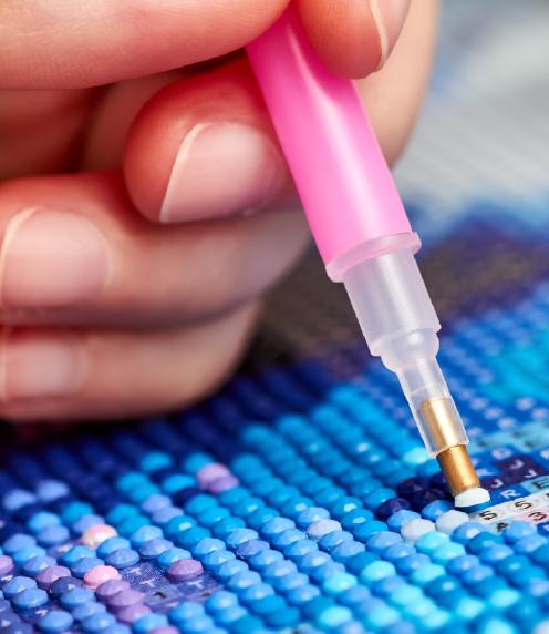 Hand of person creating a diamond painting in blues and purples