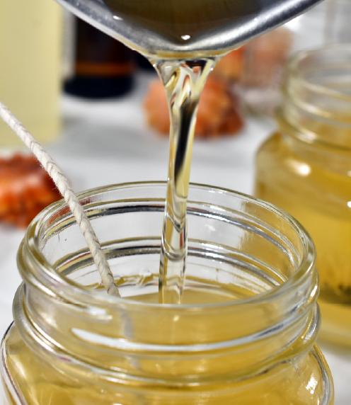 Melted wax being poured into a glass jar with a wick