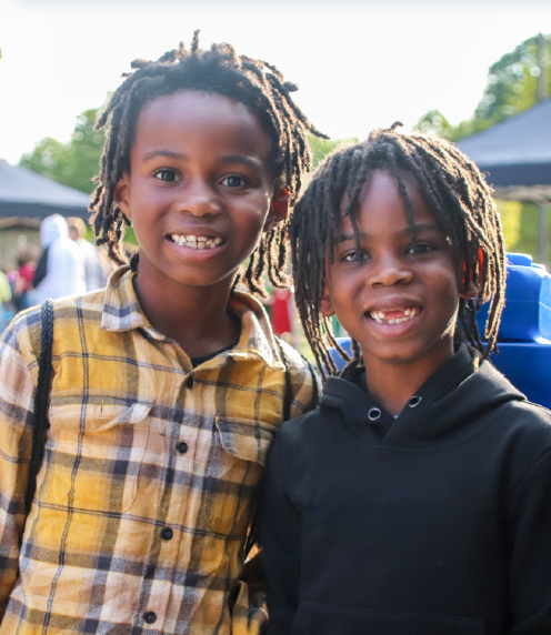 Two boys smiling at the camera, Family Learning Day vendors in the background