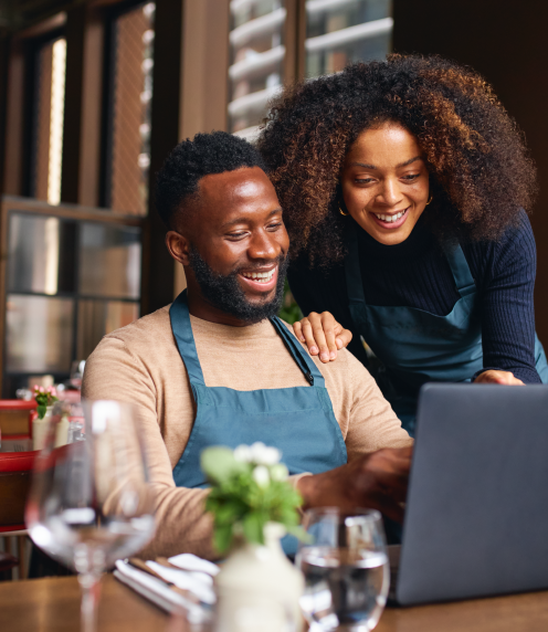 Happy man in work apron and woman looking at laptop