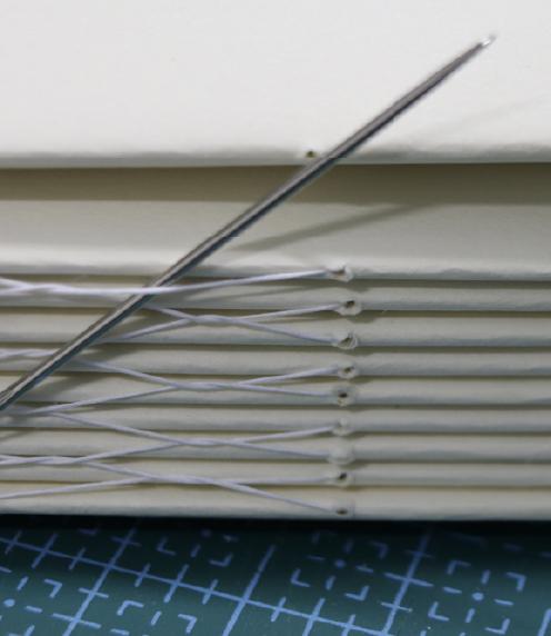 Close up of a bookbinding needle with a pile of sewn signatures