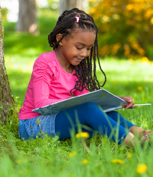 Little girl reading a book under a tree
