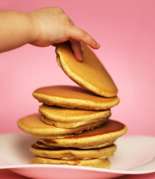 Infant hand picking up a pancake from a stack of pancakes on a plate