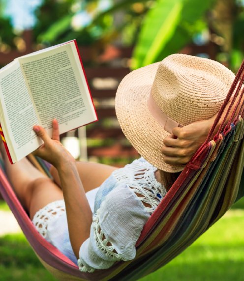Woman laying on a hammock, reading a book, photographed from behind