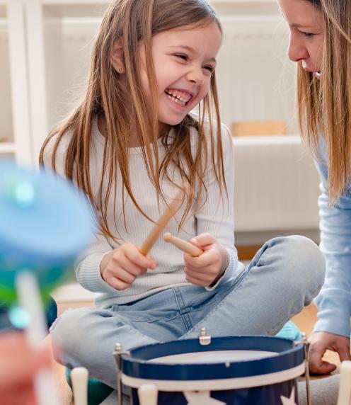 Little girl playing a drum while her mother watches