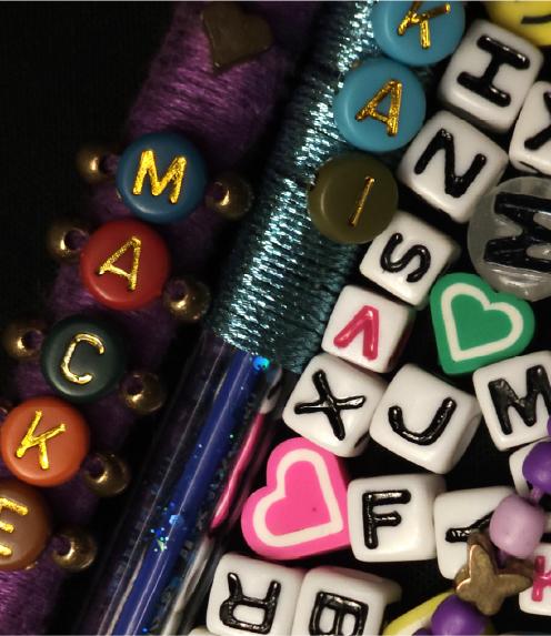 Close up of letter beads, heart beads, and two pens decorated with beads and thread