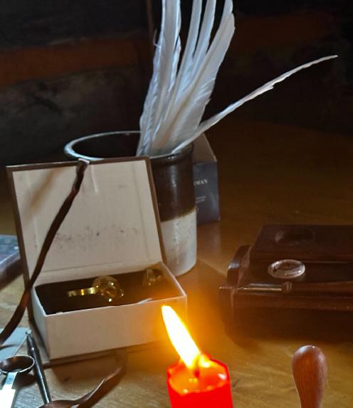 Quills in a jar, an old writing slate, and a flickering candle