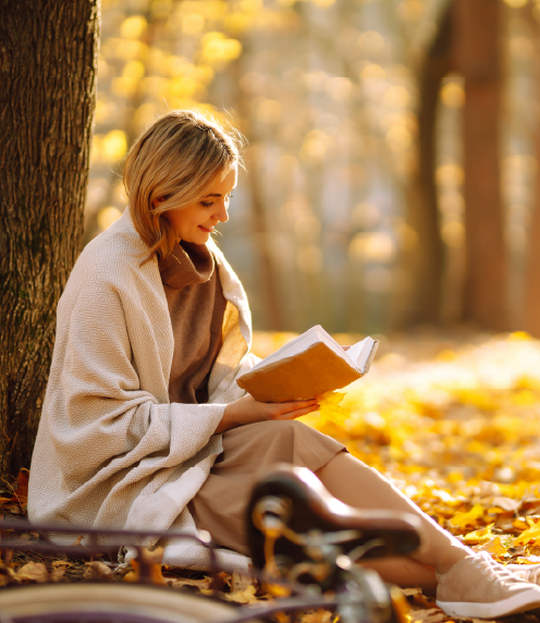 Woman reading a book while wrapped in a blanket under a tree