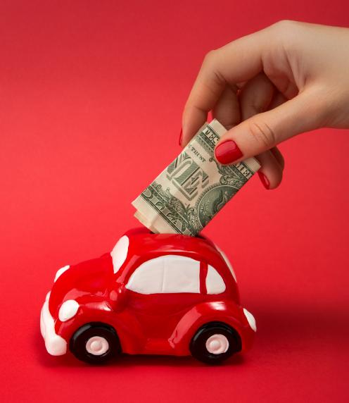 Woman placing dollar bills into a red car-shaped bank on a red background