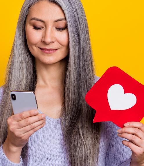 Senior woman looking at a smart phone while holding a text box that contains a heart