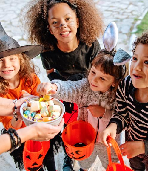 Image: A group of trick-or-treaters smiling and taking candy