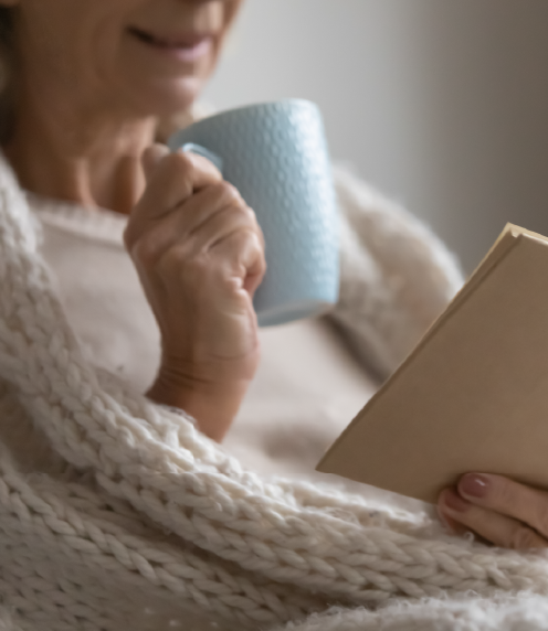 Woman wearing a cozy sweater and drinking from a cup while reading